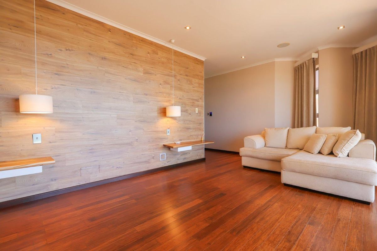 A well-maintained living room featuring warm timber flooring and a prominent wood-paneled feature wall with integrated floating shelves and pendant lighting.