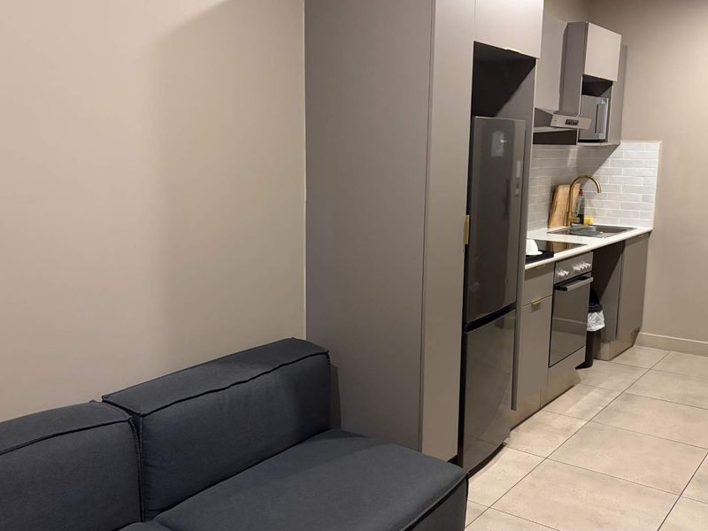 Modern open-plan kitchen featuring sleek grey cabinetry, integrated appliances, subway tile backsplash, and contemporary brass fixtures, seamlessly connected to the living area.