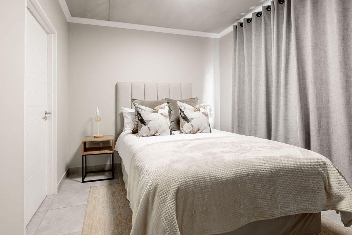 A well-maintained bedroom featuring neutral wall tones, tiled flooring, and a modern door, creating a clean and inviting living space.