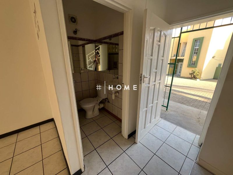 A small, functional bathroom featuring tiled walls and flooring, accessible from an exterior courtyard area.
