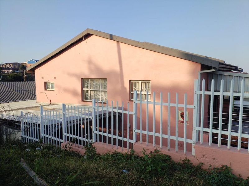 Rear view of the property featuring a pink exterior facade, metal security fencing, and security bars on the windows.