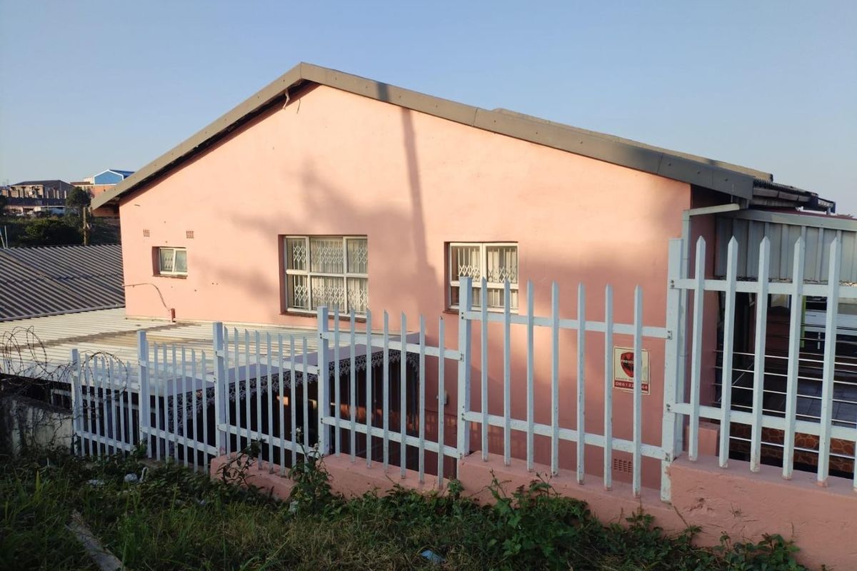 Rear view of the property featuring a pink exterior facade, metal security fencing, and security bars on the windows.