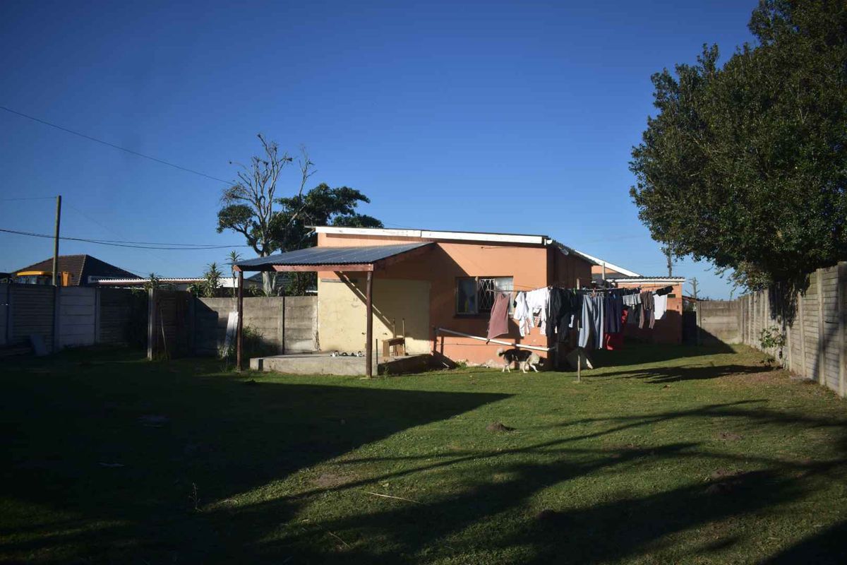 Rear view of the house featuring a small covered patio area, a spacious backyard, and perimeter concrete wall fencing.