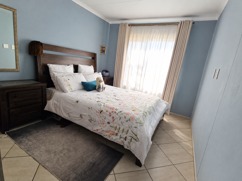 A well-maintained bedroom featuring neutral tiled flooring, light blue walls, and large windows with fitted curtain rails.