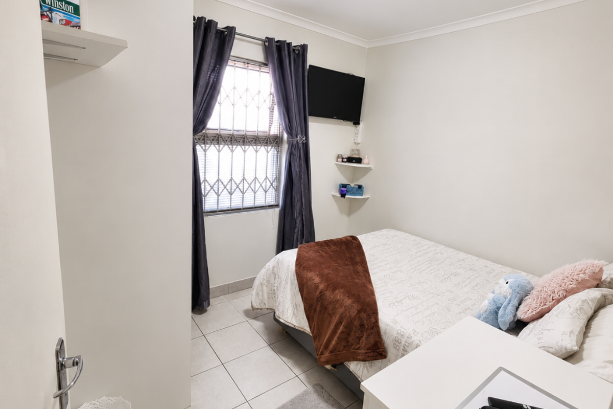 A compact bedroom featuring tiled flooring, a window with a security gate, and built-in wall shelving.