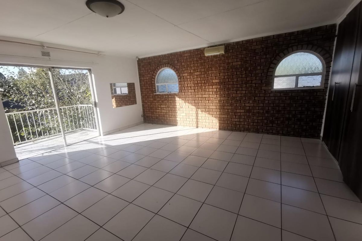 Spacious bedroom featuring an exposed brick feature wall, arched windows, tiled flooring, built-in cupboards, and direct access to a balcony through sliding glass doors.