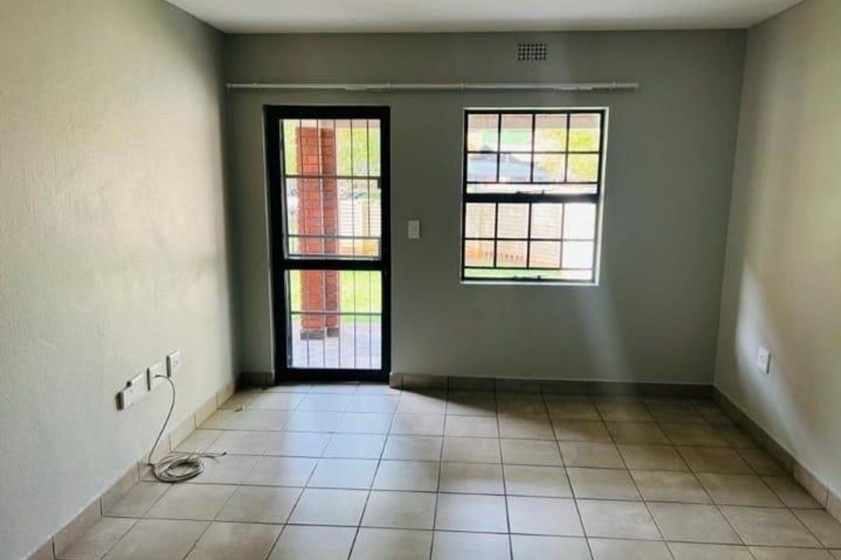 An empty living room featuring tiled flooring, a security gate leading outdoors, and a window with security bars.