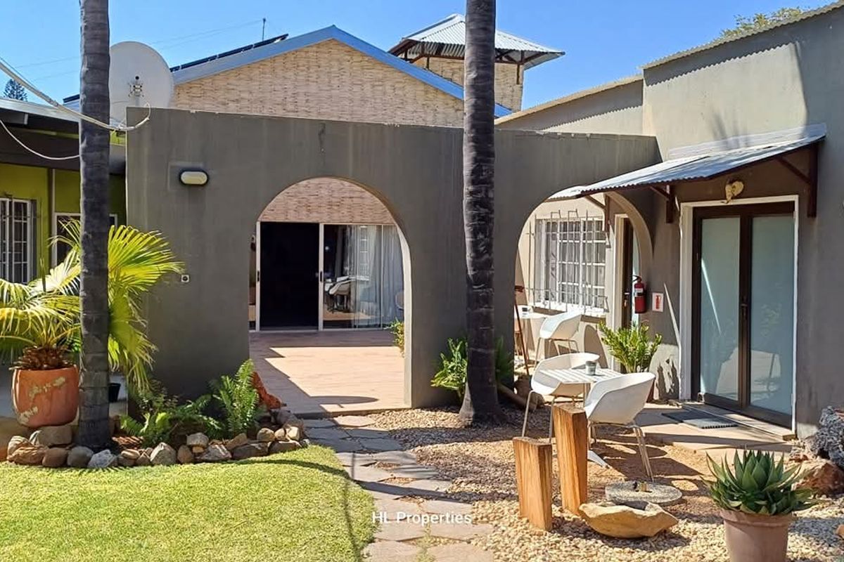 A view of the guest house rear courtyard featuring an arched walkway, paved patio area, and landscaped garden space.