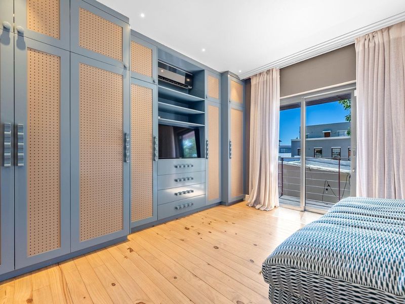 A well-appointed bedroom featuring extensive custom built-in cabinetry, light timber flooring, and direct access to a private balcony through sliding glass doors.