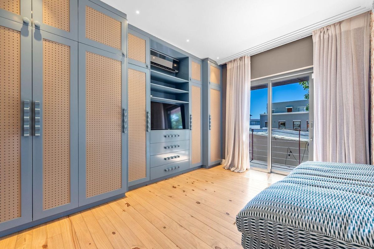 A well-appointed bedroom featuring extensive custom built-in cabinetry, light timber flooring, and direct access to a private balcony through sliding glass doors.