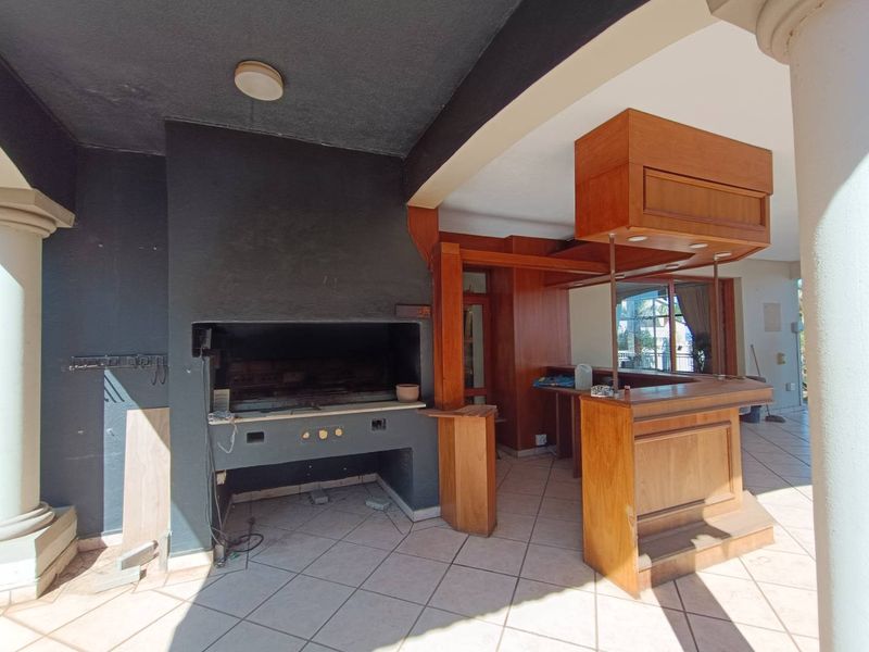 Covered outdoor patio featuring a built-in braai and a wooden bar counter, providing a functional space for outdoor entertaining.