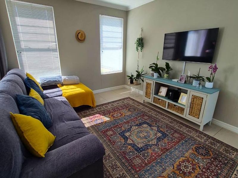A comfortable living room featuring neutral wall tones, tiled flooring, recessed downlighting, and dual windows fitted with venetian blinds.