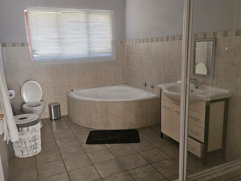 A functional bathroom featuring a corner bathtub, separate shower enclosure, vanity cabinet with basin, and neutral tiled finishes throughout.