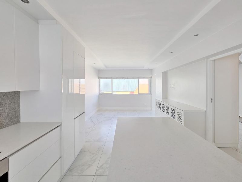 A bright, modern open-plan living and kitchen area featuring sleek white cabinetry, stone countertops, and polished marble-look floor tiles throughout.
