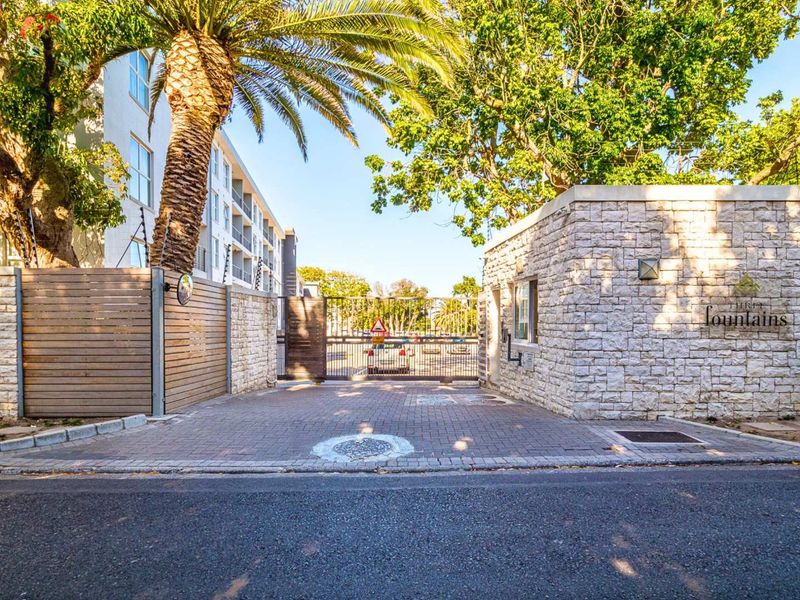 Secure gated entrance to the Three Fountains apartment complex, featuring stone-clad walls, paved driveway, and electric fencing for enhanced security.