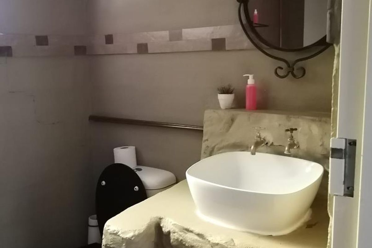 A rustic-style bathroom featuring a custom stone-effect vanity base, a modern vessel sink, and a wall-mounted mirror.