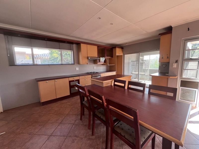 Open-plan kitchen and dining area featuring wooden cabinetry, built-in appliances, tiled flooring, and direct access to an outdoor patio through sliding glass doors.