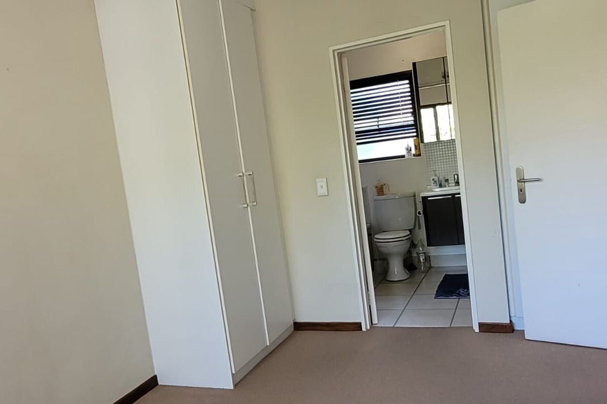 A spacious bedroom featuring neutral carpet flooring, a built-in wardrobe, and direct access to an en-suite bathroom.