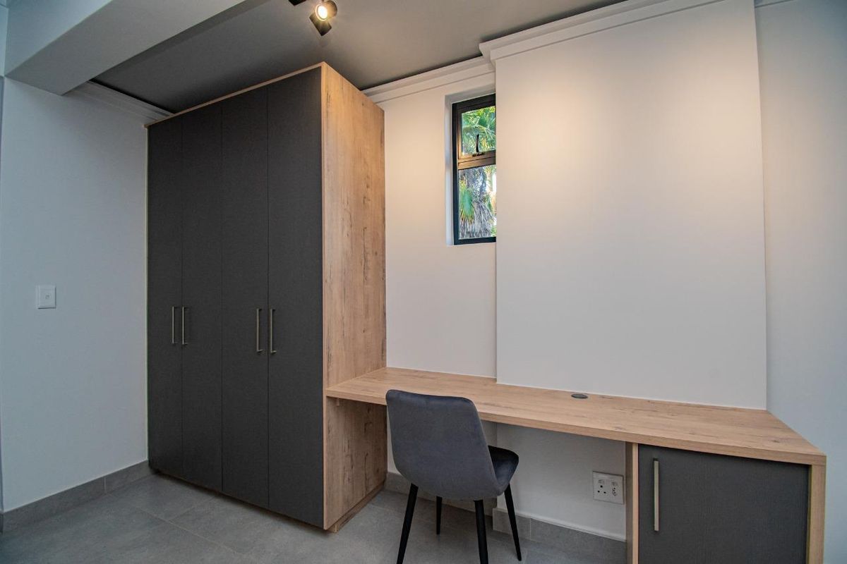 A modern bedroom featuring built-in dark grey and wood-grain cabinetry with an integrated desk workspace and tiled flooring.