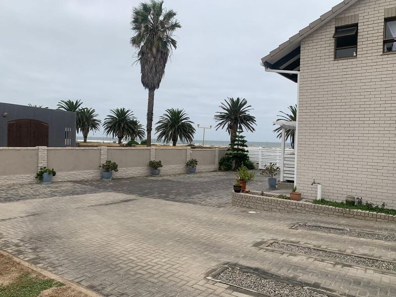 A view of the exterior side and rear area featuring paved driveway, perimeter boundary wall, and established palm trees with a coastal outlook.
