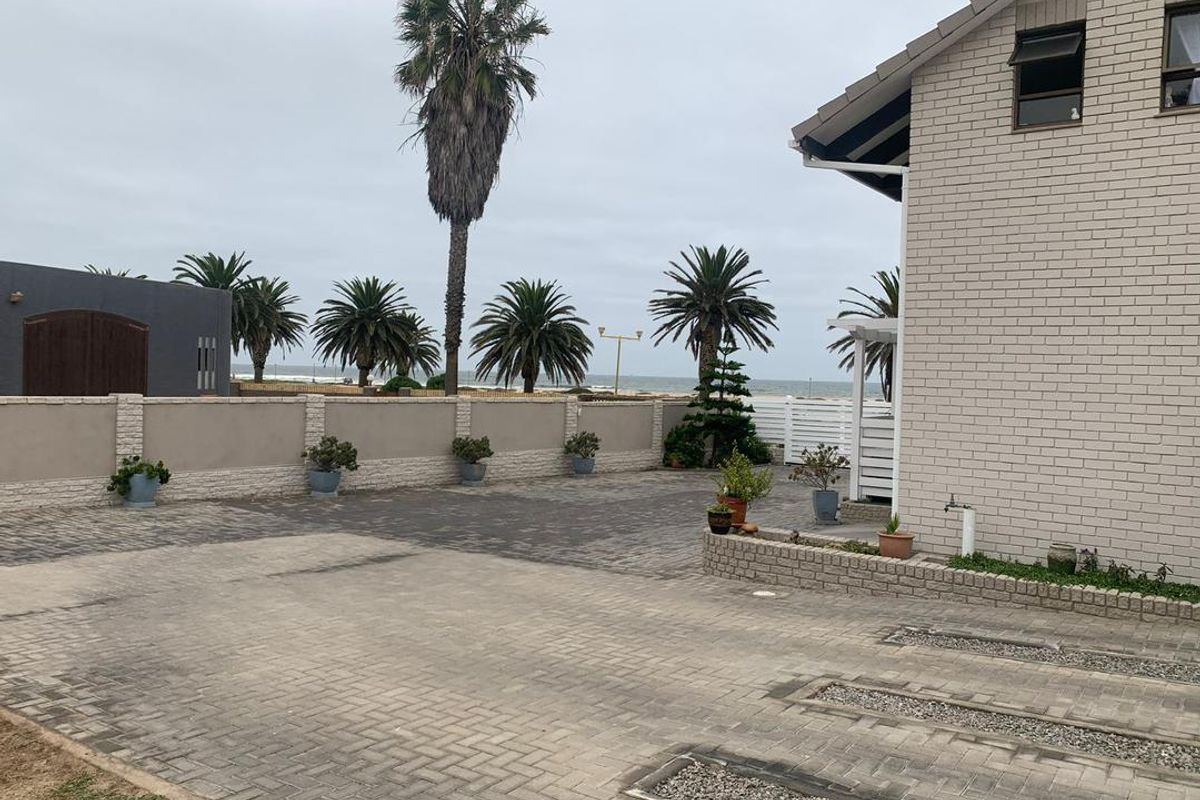 A view of the exterior side and rear area featuring paved driveway, perimeter boundary wall, and established palm trees with a coastal outlook.
