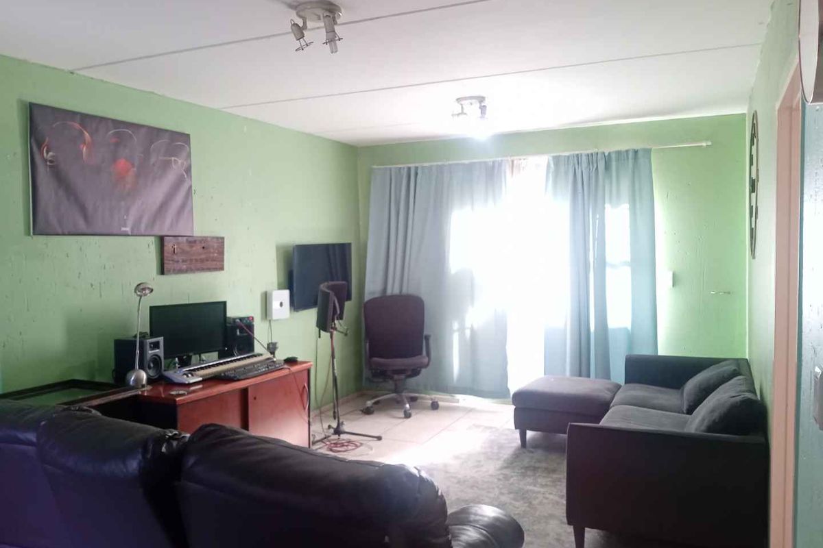 A living room area featuring tiled flooring and a sliding door providing natural light access, currently used as a multi-purpose living and workspace.