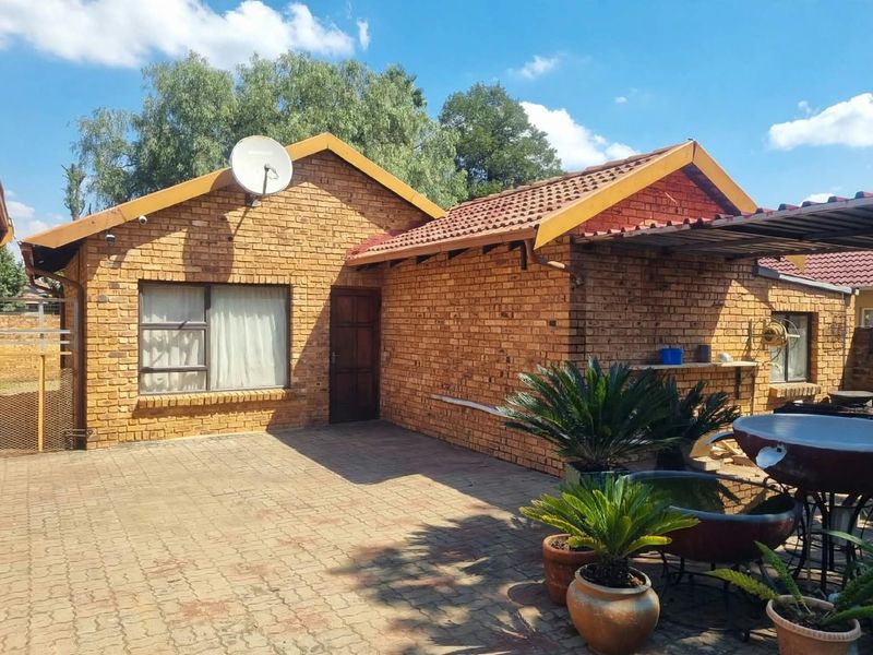 Rear view of a face brick house featuring a paved patio area, tiled roof, and satellite dish installation.
