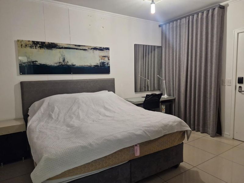A functional bedroom featuring tiled flooring, neutral wall finishes, and floor-to-ceiling curtains, providing a comfortable and practical living space.