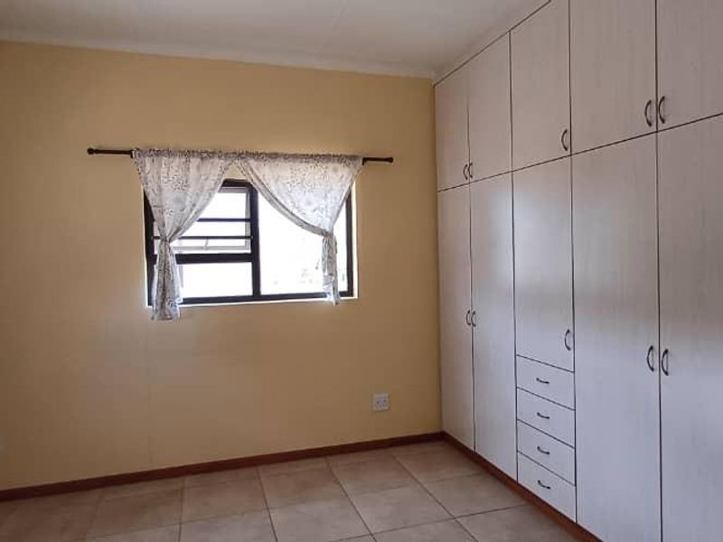 A clean, empty bedroom featuring neutral walls, tiled flooring, and extensive built-in cupboard storage space.
