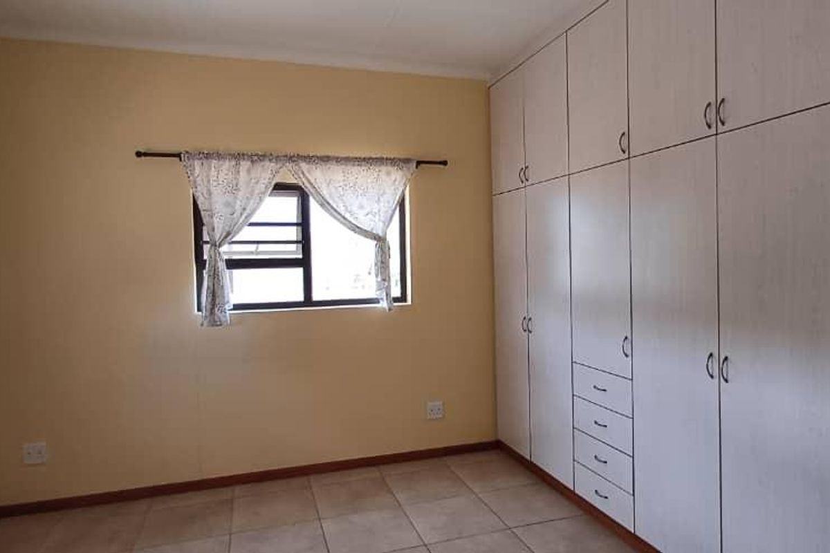 A clean, empty bedroom featuring neutral walls, tiled flooring, and extensive built-in cupboard storage space.