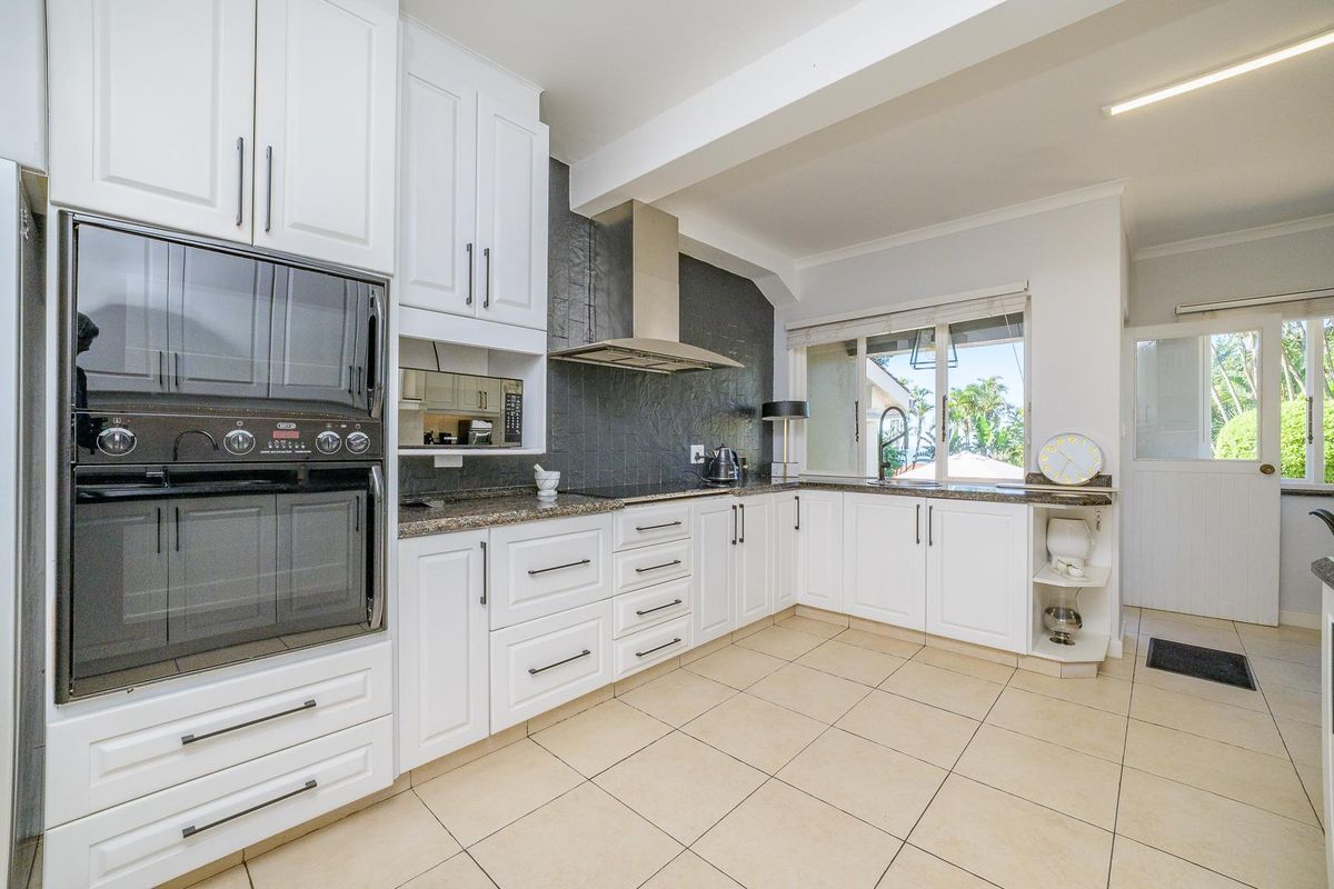 A well-maintained kitchen featuring white cabinetry, granite countertops, a built-in double oven, stainless steel extractor fan, and tiled flooring.