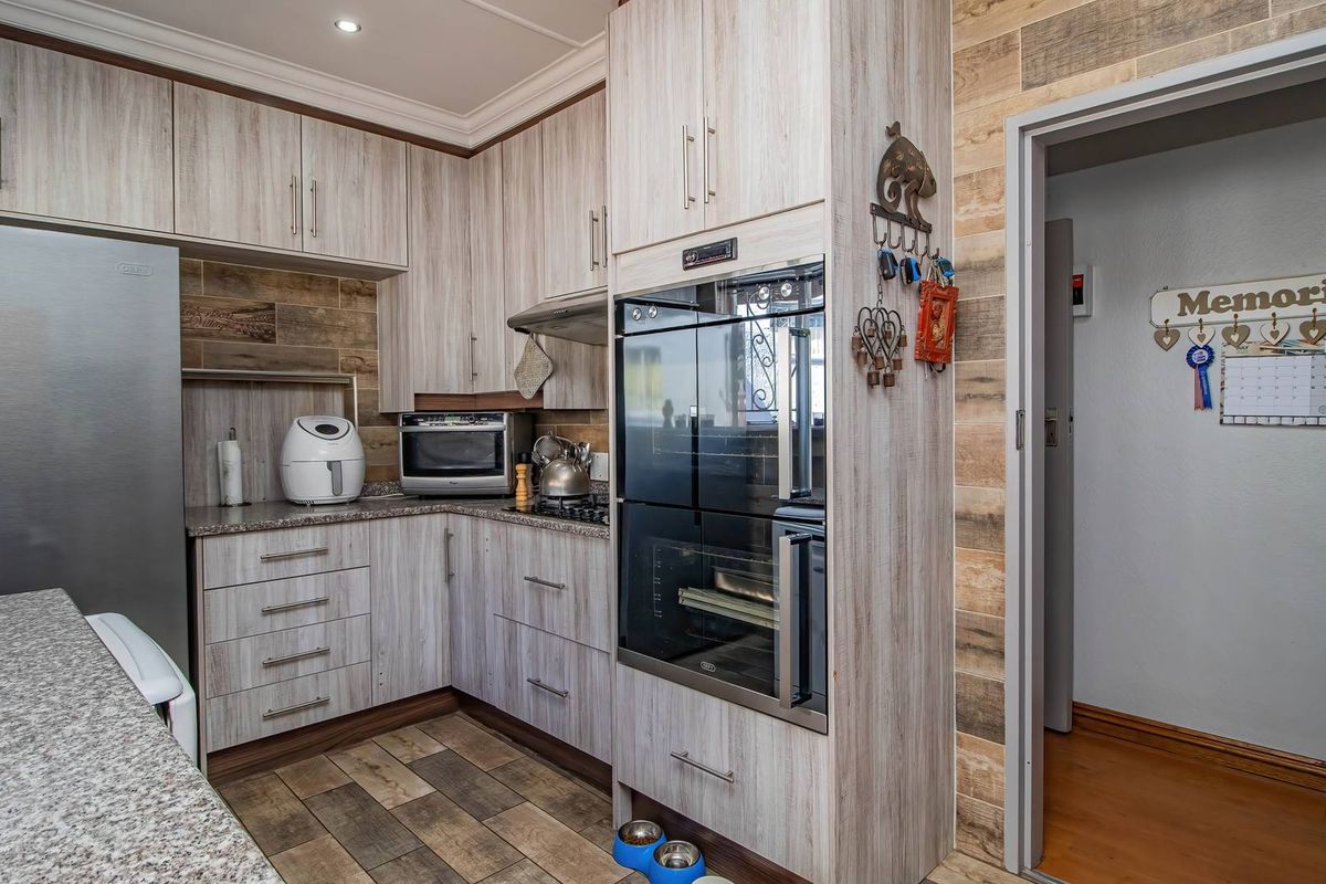 Modern kitchen featuring light wood-grain cabinetry, granite countertops, built-in oven, extractor fan, and stylish tiled flooring with a seamless transition to the adjacent hallway.