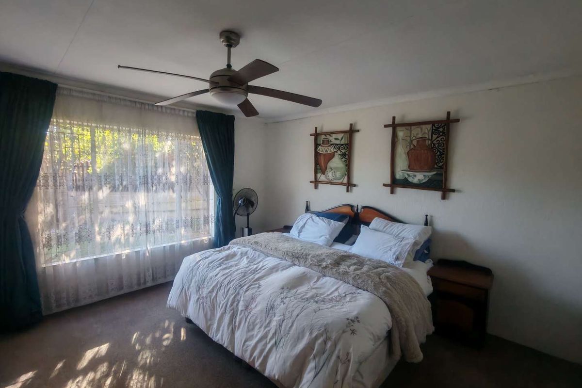 A standard bedroom featuring a ceiling fan and carpeted flooring, offering a functional space with natural light from the window.