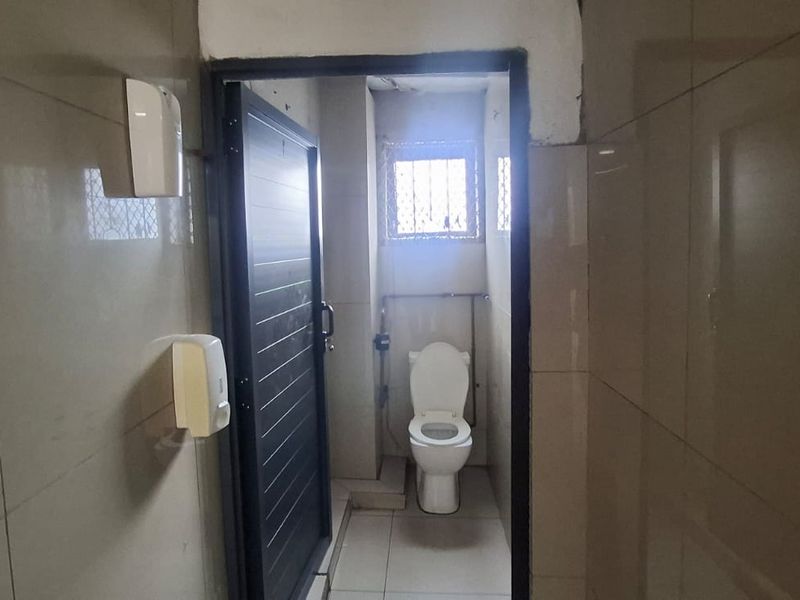 A functional bathroom featuring tiled walls and flooring, equipped with a standard toilet and security window grille.