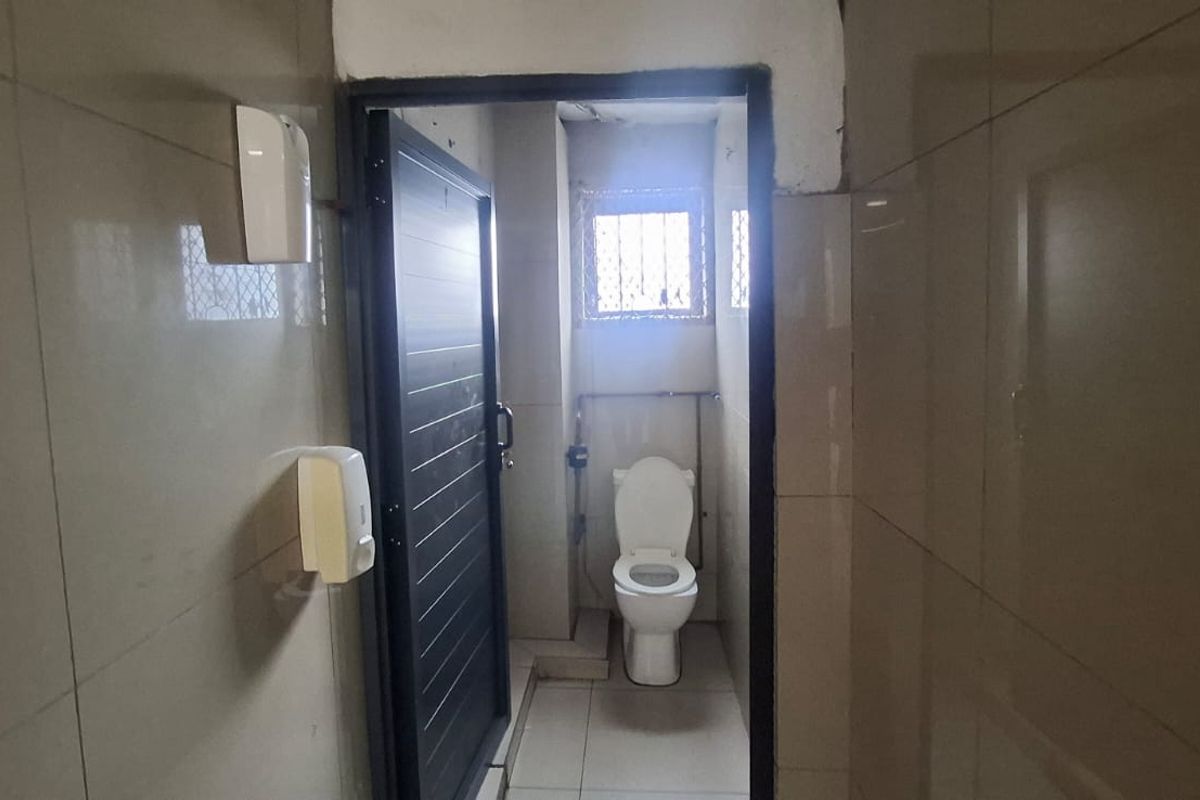 A functional bathroom featuring tiled walls and flooring, equipped with a standard toilet and security window grille.
