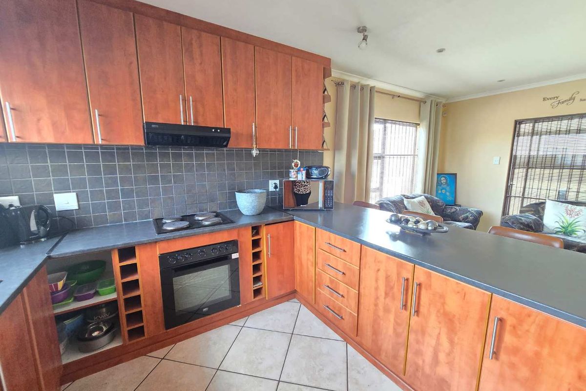A functional kitchen featuring wood-tone cabinetry, a dark countertop, built-in oven, hob, and extractor fan, with tiled flooring throughout.