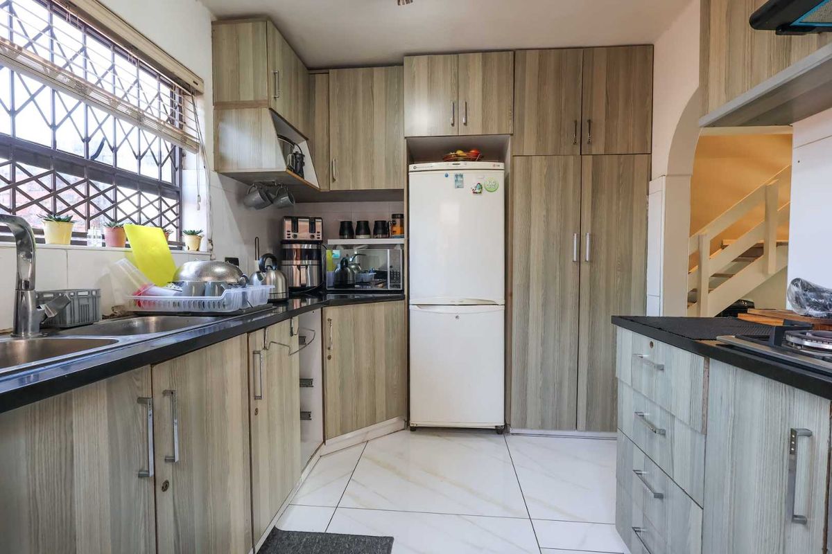 Functional kitchen featuring wood-look cabinetry, dark countertops, double basin sink, and tiled flooring, with an adjacent staircase visible.