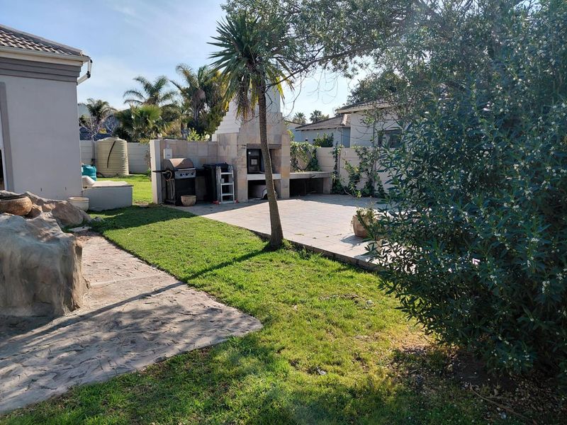 Rear garden area featuring a paved patio, built-in braai, and established landscaping, providing a functional outdoor entertainment space.