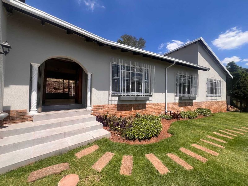 Front elevation of the house featuring a brick and plaster facade, arched entrance with decorative columns, security bars on windows, and a landscaped garden.