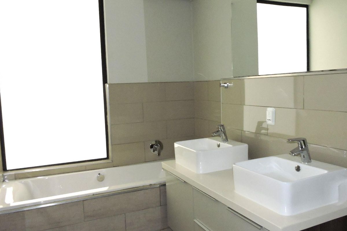 Modern bathroom featuring a double vanity with vessel sinks, a built-in bathtub, and large wall-mounted mirrors with neutral tiled finishes.