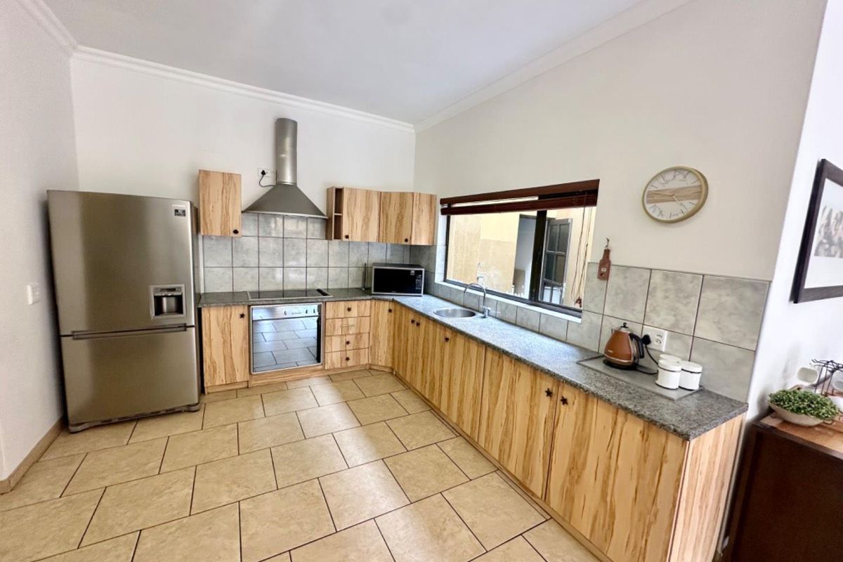 A functional kitchen featuring light wood-grain cabinetry, granite countertops, tiled backsplash, stainless steel extractor fan, and built-in oven with ceramic hob.