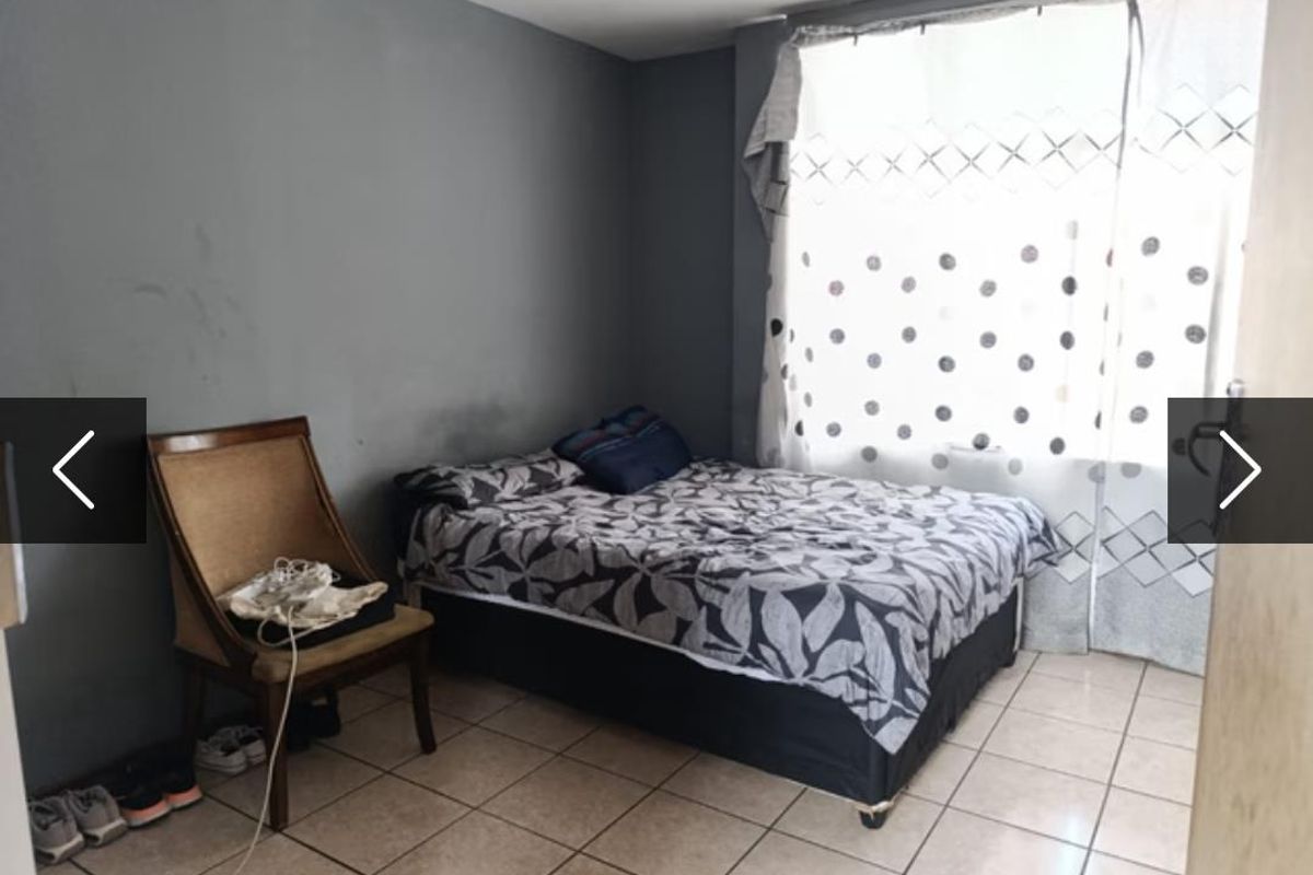 A bedroom featuring tiled flooring and a large window, currently requiring cosmetic updates to the wall finishes.