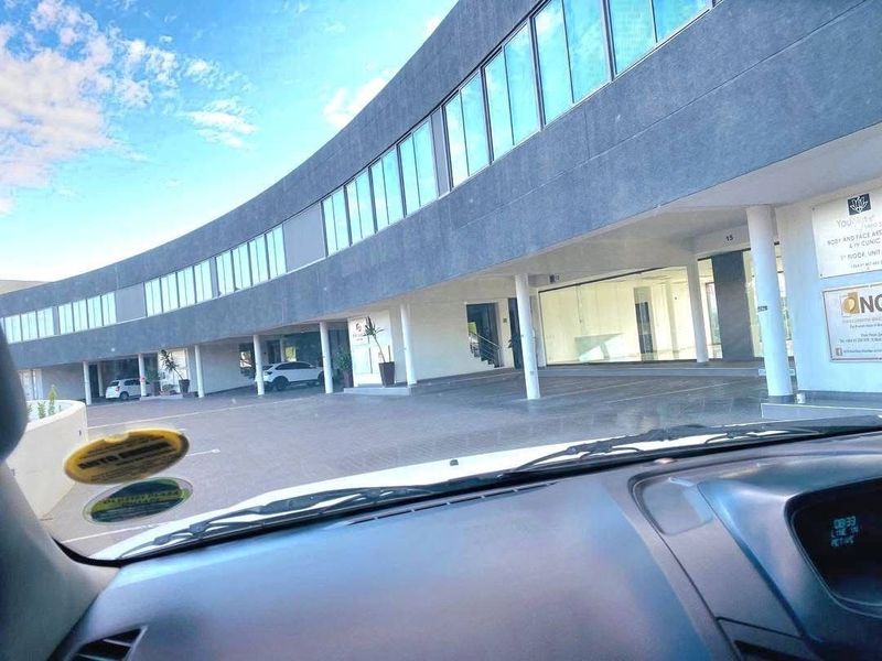 Modern commercial building with a distinctive curved facade, glass windows, and a covered ground-level parking area.