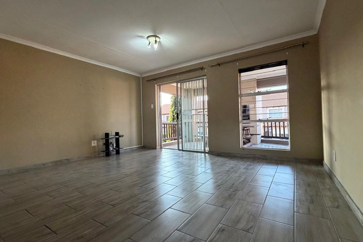 Spacious living area featuring modern wood-look floor tiles, neutral wall tones, and direct access to a private balcony through a sliding glass door.