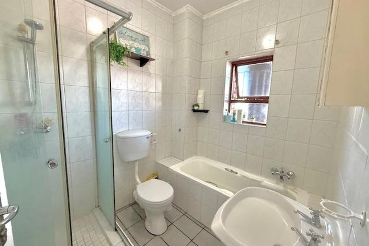 A functional bathroom featuring a separate shower enclosure, a bathtub, a pedestal sink, and a toilet, finished with full-height wall tiling.