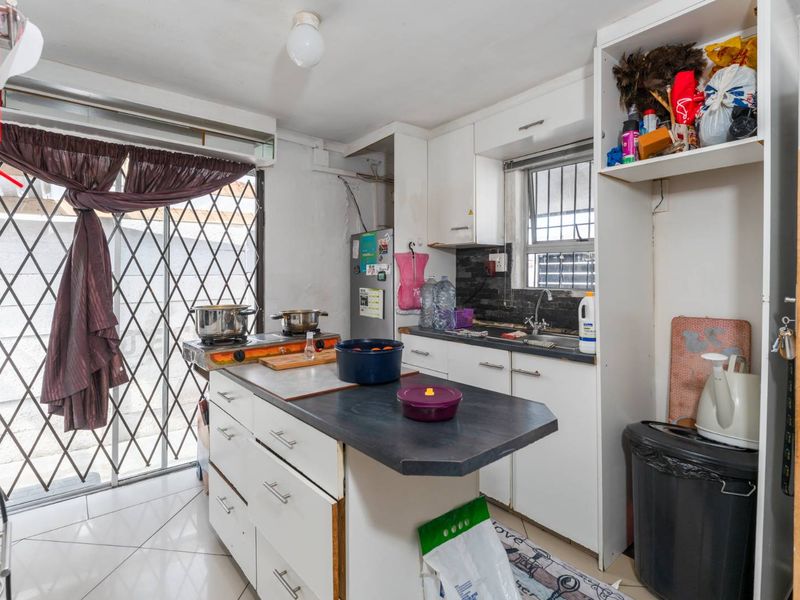 A compact kitchen featuring a central island, white cabinetry, tiled flooring, and a security gate leading to the exterior.