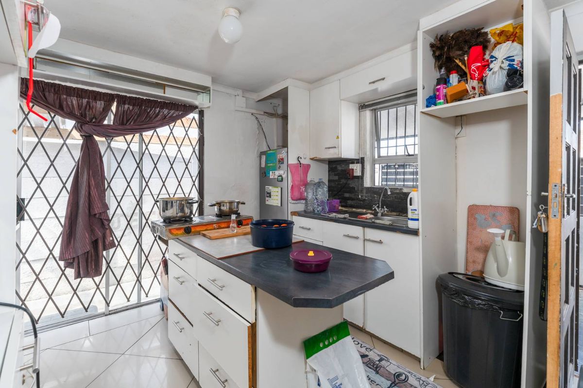 A compact kitchen featuring a central island, white cabinetry, tiled flooring, and a security gate leading to the exterior.
