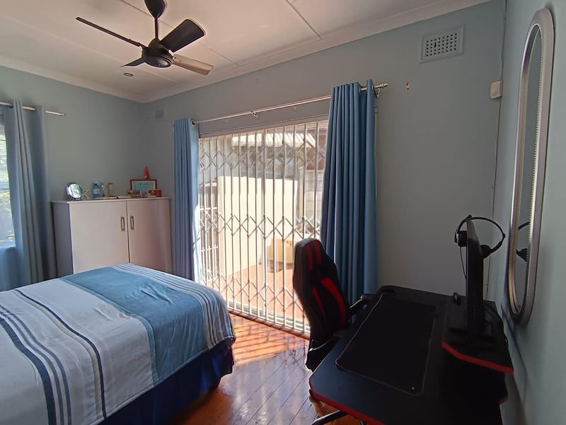 A well-maintained bedroom featuring hardwood flooring, a ceiling fan, and a sliding glass door with a security gate providing access to the exterior.