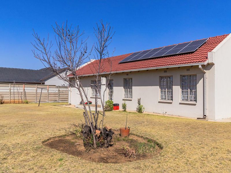 Rear view of the house featuring a tiled roof with installed solar panels, security bars on windows, and a spacious backyard with boundary walling.