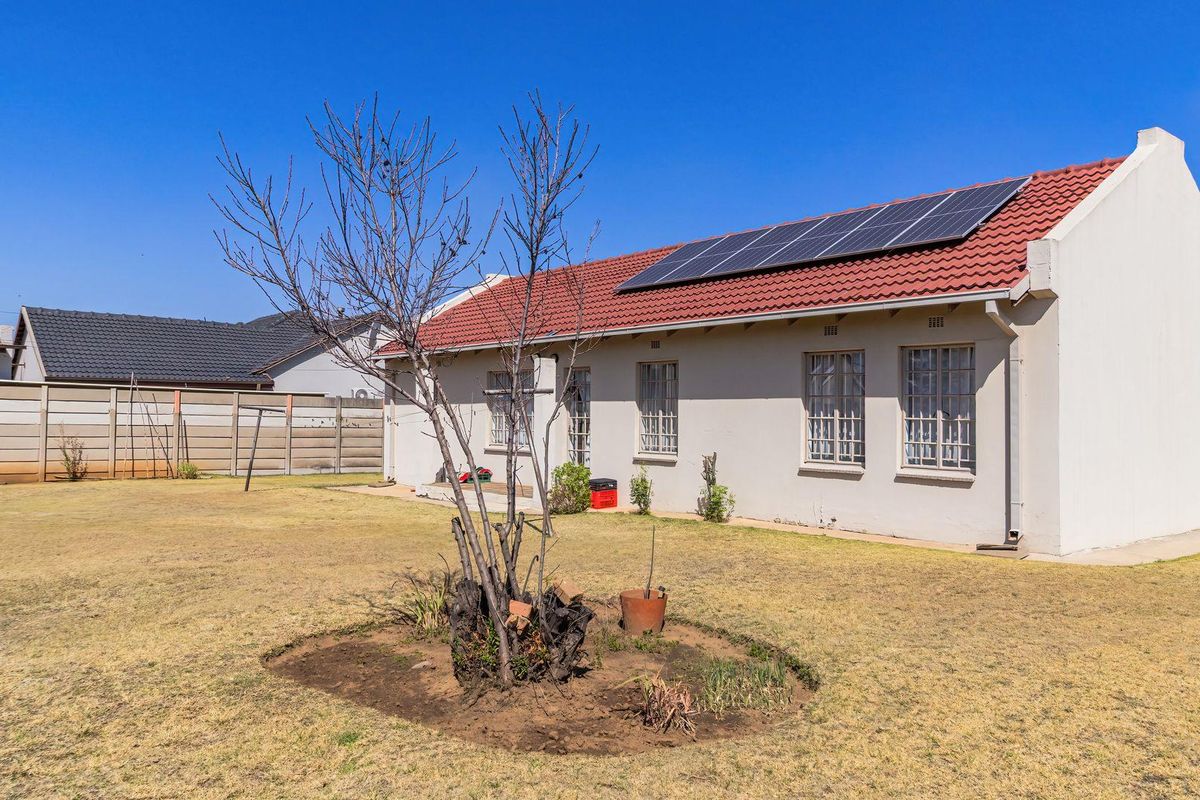 Rear view of the house featuring a tiled roof with installed solar panels, security bars on windows, and a spacious backyard with boundary walling.